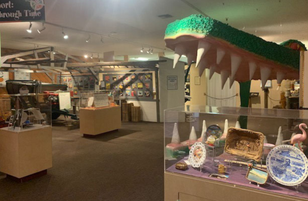 A dinosaur model peering curiously into a museum exhibit, amidst an array of artifacts and displays.