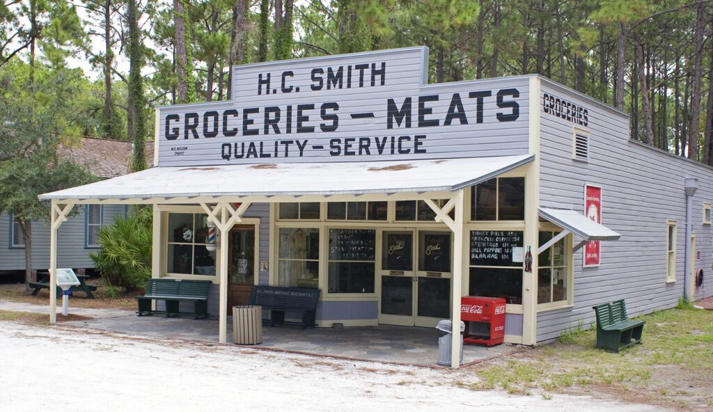 Vintage-style grocery store with a sign reading "h.c. smith groceries - meats quality - service" set amongst pine trees.
